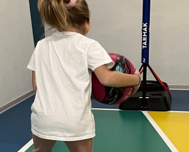 Bambina che gioca con un pallone su un campo multisport nella palestra Move 2 Grow a Milano, utilizzando cerchi colorati