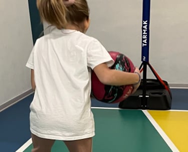 Bambina che gioca con un pallone su un campo multisport nella palestra Move 2 Grow a Milano, utilizzando cerchi colorati
