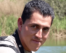 Headshot of Chiapas birding guide Eric Lopez Villanueva wearing binoculars with lake in background