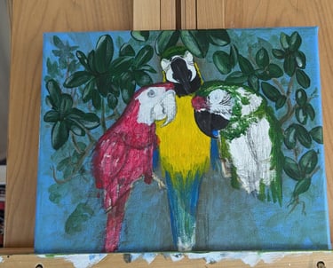 Progress photo of three macaws painting on a wooden easel.