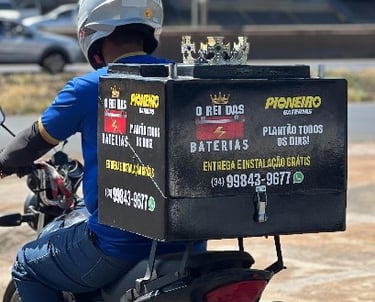 Um entregador segura uma bateria da Disk Baterias Uberlândia em frente a um carro amarelo.