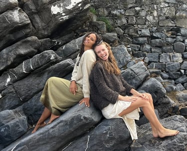 Two women sitting back to back on a rock.