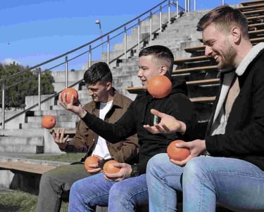 Trys jauni vyrai sedi ir meto apelsinus