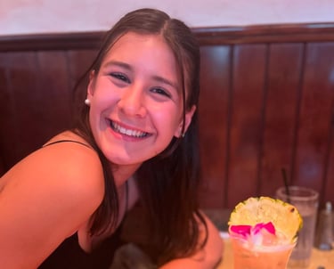 A girl smiling while at a table drinking a drink