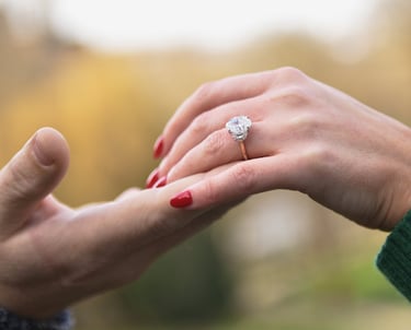 gros plan sur un main d'homme soulevant la main d'une femme portant une bague de fiançailles, le fond est lumineux et flou.