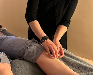 Acupuncturist inserting needle into patient’s lower leg on acupuncture table. 