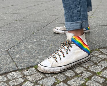 Foto von weißen Turnschuhen mit Regenbogenaufdruck und Regenbogenschnürsenkeln.