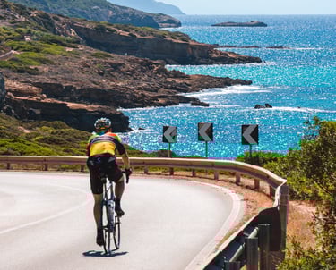Cyclist on the scenic Alghero-Bosa road in Sardinia with Mediterranean sea view.