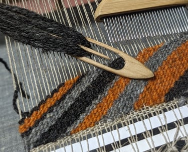 a weaving loom with shuttle, combe and black grey orange wool diagonal threads on a navajo rug in pr