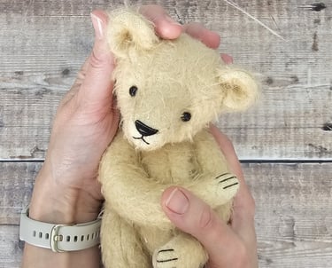 a small, pale handmade teddy bear held in hands