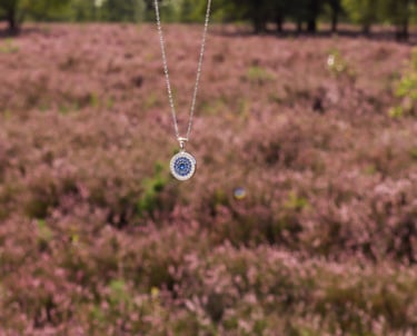 HeideSchmuck Silberkette mit rundem blauen Medaillon, gehalten vor blühender Heide in der Natur.
