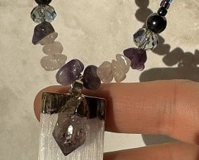 A crystal necklace with a shiny pendant made from selenite with an amethyst fixed on top