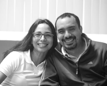 Un hombre y una mujer sentados uno junto al otro en un sofá, sonrientes miran la cámara