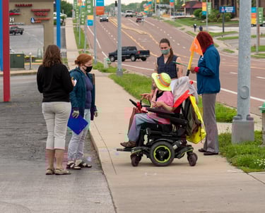 Group gathered on the sidewalk of a busy street