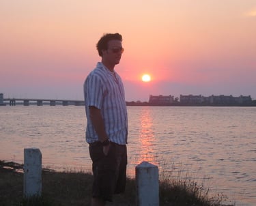 A man standing in front of the ocean with a sunset
