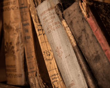 Aged books leaning against one another on a shelf
