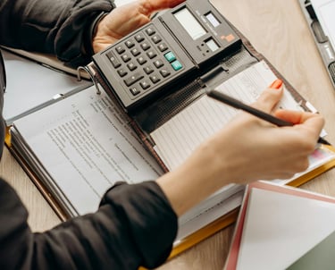 Mãos usando calculadora e caneta sobre documentos para análise fiscal e tributária