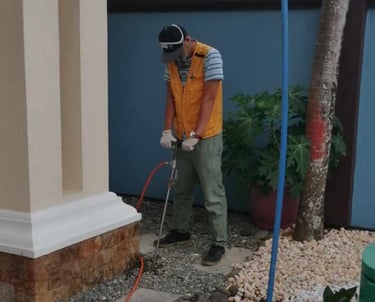 Professional pest control technician performing termite soil treatment at a residential building foundation.