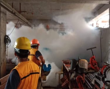 Construction workers in safety vests and hard hats monitoring a fogging machine inside a building site.