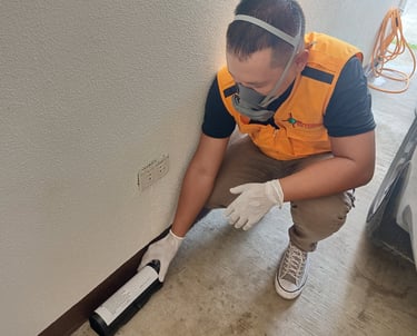 Professional pest control technician in safety gear applying termite treatment along a garage wall.