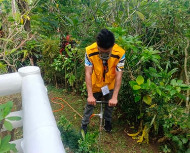 A pest control professional in a yellow vest performs soil treatment for termites in a garden.