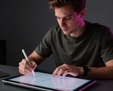 A lifestyle shot of a creative professional in a dark studio using a stylus on a large digital tablet, with soft magenta lighting on their face.