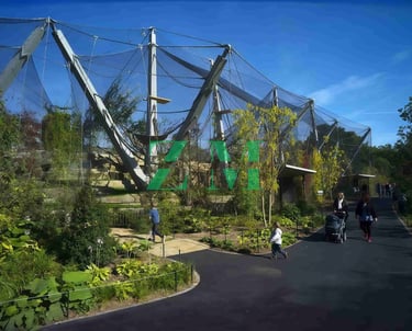 Visitors walk past the modern mesh Snowden Aviary at the London Zoo under a clear blue sky.