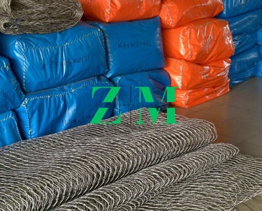 Rolls of stainless steel wire rope mesh in front of orange and blue packaged zoo fencing.