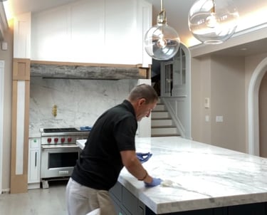 Professional contractor sealing a white marble kitchen island countertop during a home renovation.