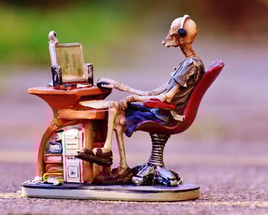 Skeleton figurine wearing a headset and sitting at a miniature computer desk gaming setup.