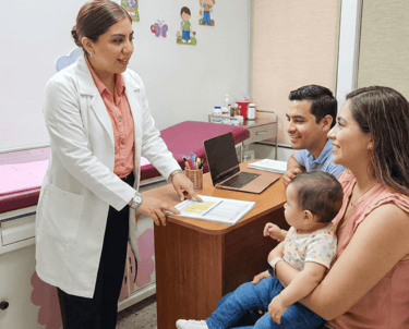 Una pediatra con bata blanca consulta con unos padres y su bebé en una clínica médica.