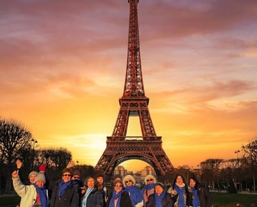 Un grupo de turistas con bufandas azules posan frente a la Torre Eiffel durante una puesta de sol.