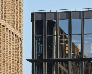 Modern office building facade featuring textured brown brick and glass windows.