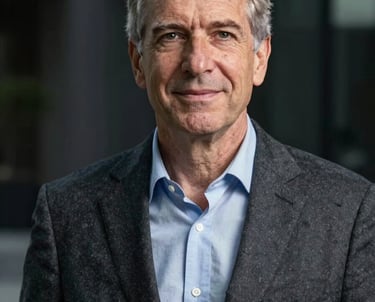 A professional headshot of a senior technology executive in a charcoal blazer, standing against a dark architectural background. North American / International.