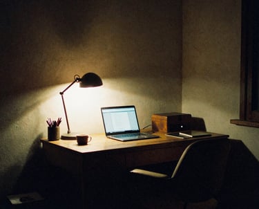 A cozy home office workspace featuring a laptop and desk lamp illuminating a wooden desk at night.