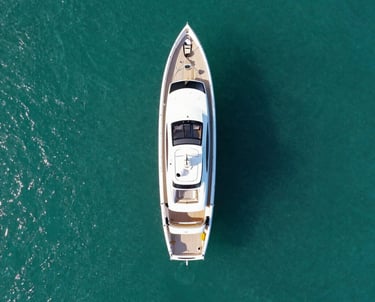 An aerial drone shot of a luxury yacht in a turquoise ocean. The composition is clean and premium, showing the scale of the landscape. Global / International.