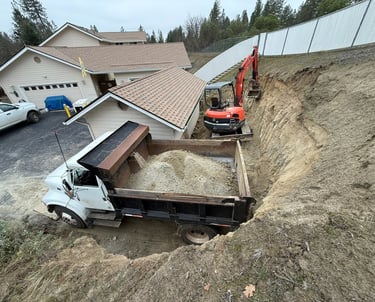 Excavator digging around building, dump truck full of dirt in front