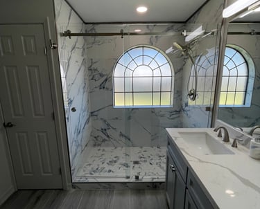 Modern master bathroom remodel featuring a walk-in marble shower with glass doors and arched window.