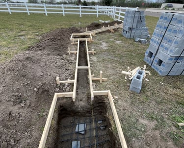 Concrete foundation forms and rebar prepared for a residential fence installation with cinder blocks.