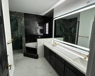 Modern master bathroom with white marble floors, a double vanity, and a black accent tile shower.