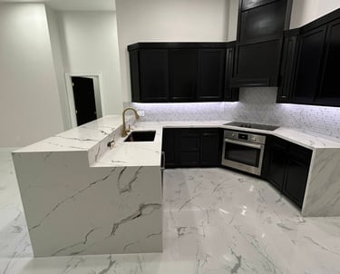 Modern luxury kitchen featuring black cabinets, white marble waterfall island, and matching marble flooring.