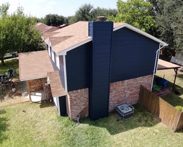 Aerial view of a suburban home featuring navy blue siding, brick exterior, and a new brown shingle roof.