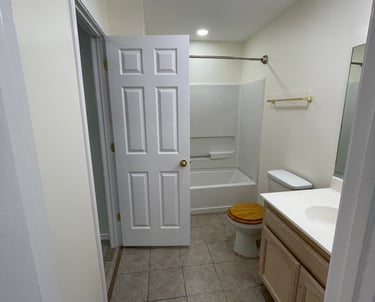 A modern bathroom remodel featuring a neutral tile floor, white bathtub, and light wood vanity.