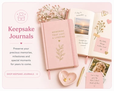 Pink keepsake journals with gold foil lettering, flowers, and scrapbooking photos on a desk.