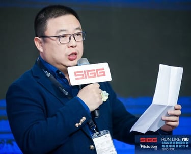 A man in a blue blazer speaking into a SIGG microphone while holding notes at an ISPO Beijing event.