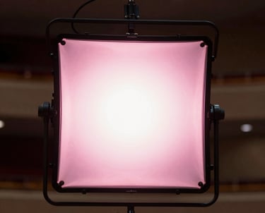 High-resolution photography of a professional lighting rig hanging in a North American / US auditorium, glowing with soft pink light.