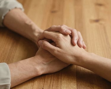 A close up of two people in a North American setting holding hands across a wooden table, emphasizing human touch and the bond of companionship. Warm gold lighting and a gentle, safe atmosphere.