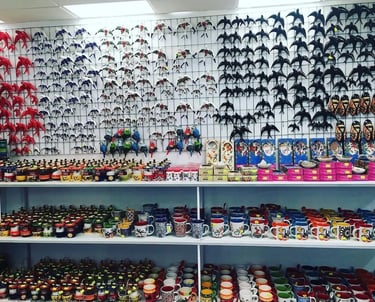 A colorful souvenir shop display featuring ceramic bird figurines and patterned coffee mugs on shelves.