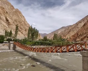 Orange suspension footbridge crossing a river in a rocky mountain valley landscape.