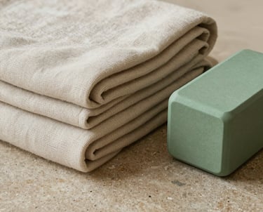 An elegant detail shot of organic woven textiles, presenting clean folded linen blankets and a modern sage green yoga block resting on a polished sandstone surface. Premium aesthetic showing sustainable luxury and mindfulness. Global / South Asian context.